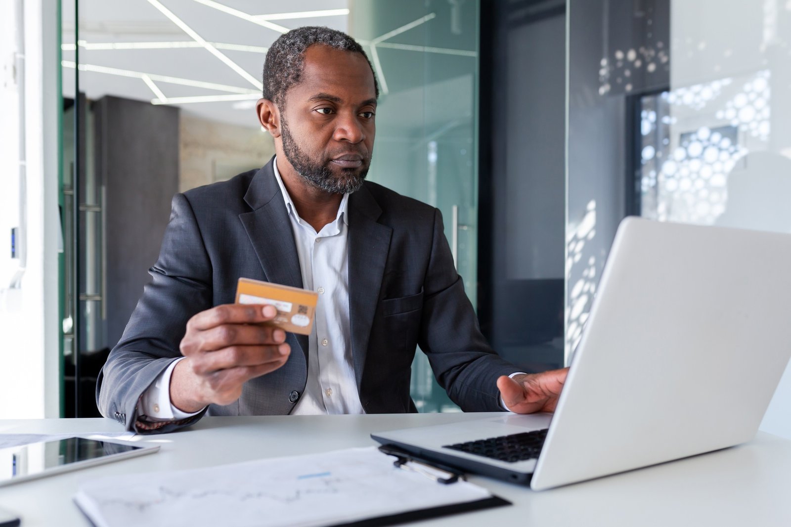 Serious thinking man in business suit working with laptop inside office, boss holding bank credit