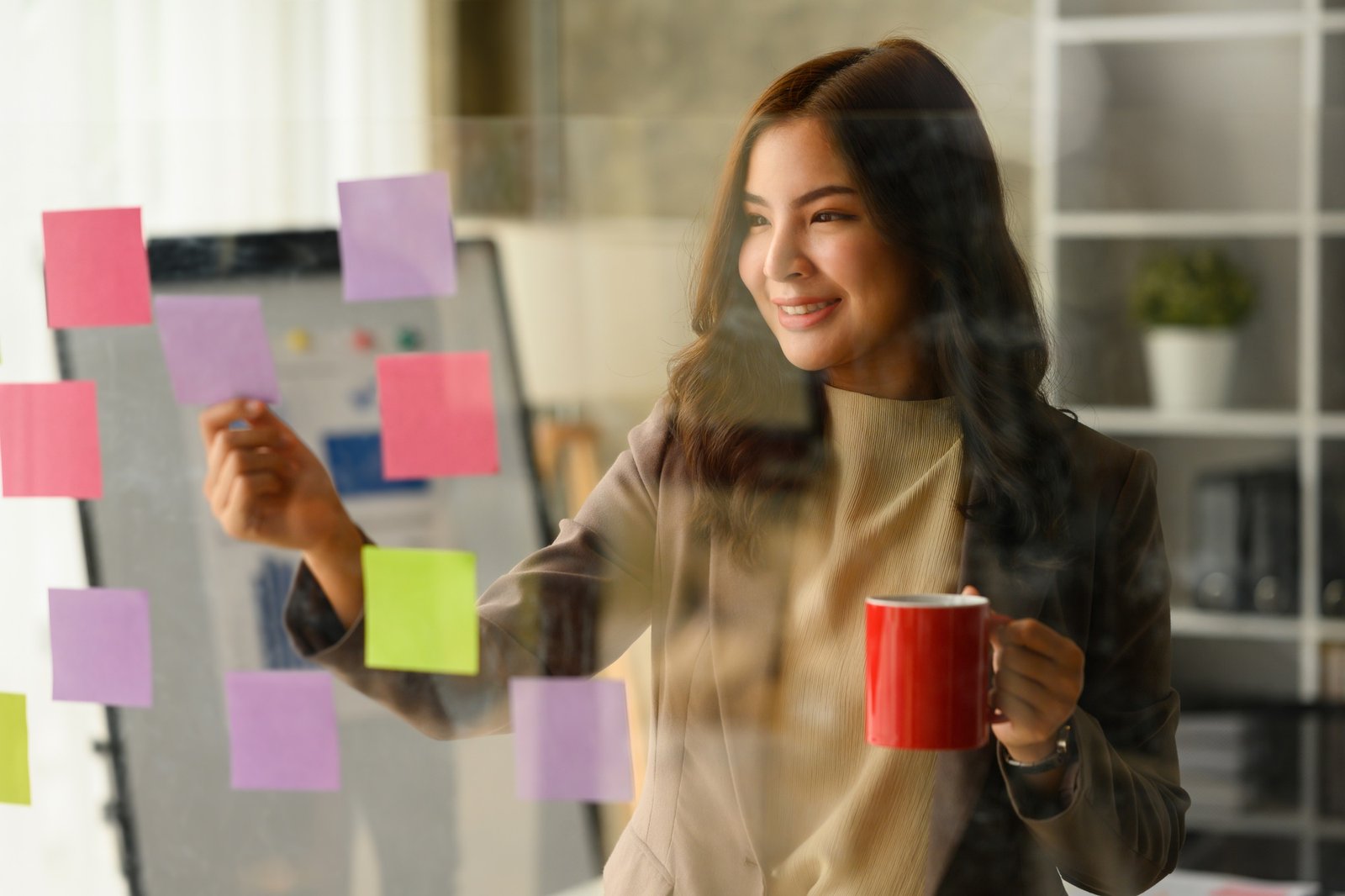 Successful startup founder drinking coffee and reading sticky notes on glass wall.