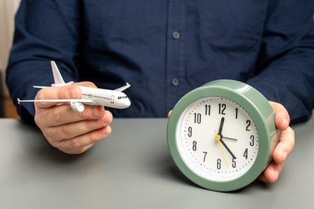 A man holds a passenger plane and a clock. Flight time. Planning a route with transfers.