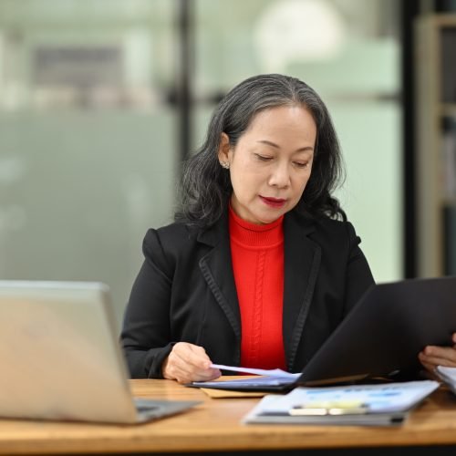 Professional senior woman accounting manager checking financial documents at workplace